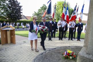 Elus déposant une gerbe de fleurs au pied d'un monument. En arrière plan, du public et des porte-drapeaux.