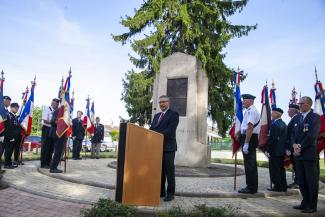 Cérémonie : discours d'un élu entouré de porte-drapeaux. En arrière plan un monument commémoratif.