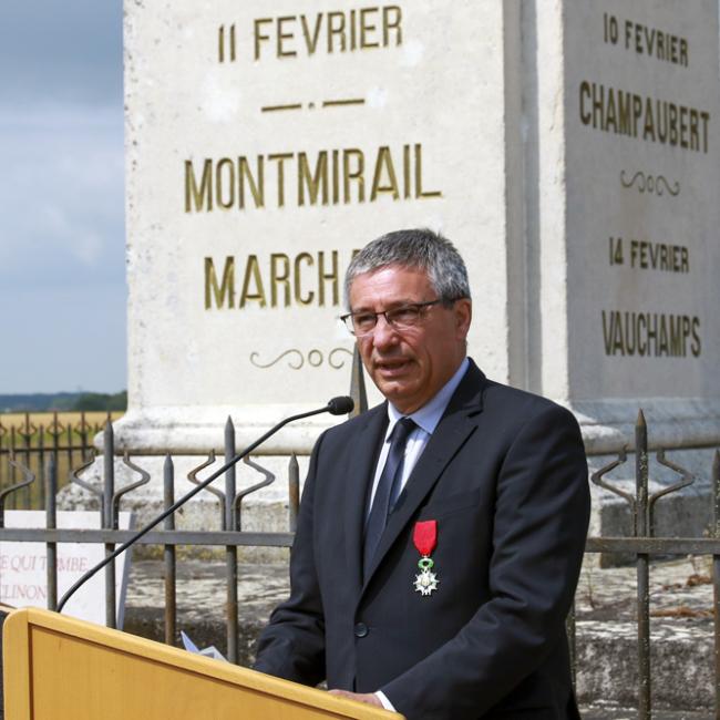 Elu devant un pupitre. En arrière-plan un monument commémoratif.
