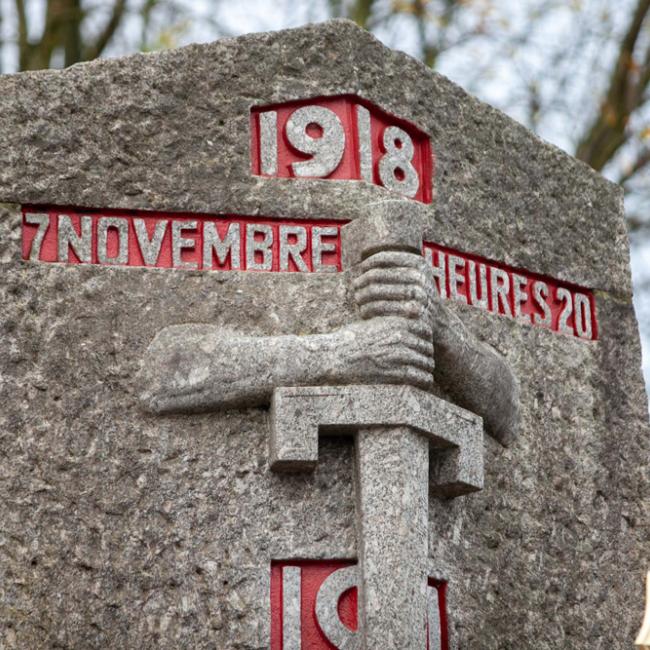 Détail d'un monument aux morts : bras tenant une épais. Inscription en rouge : 1918 7 novembre heures 20