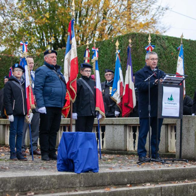 Discours devant un monument en pierre : porte-drapeaux écoutant le président du conseil départemental