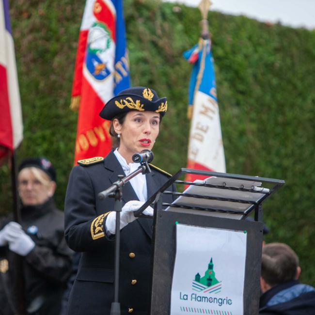 Discours de Mme la Préfète : en tenue de cérémonie officielle, en arrière plan des porte-drapeaux