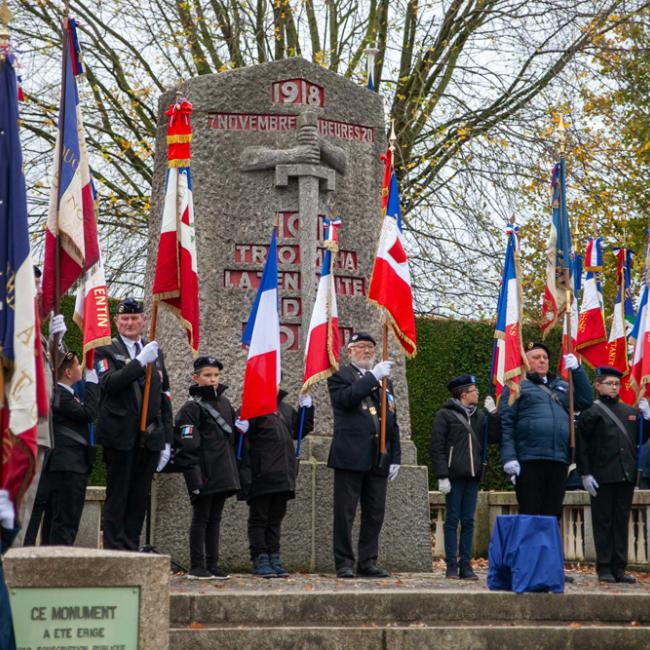 cérémonie avec des porte-drapeaux devant un monument aux morts 