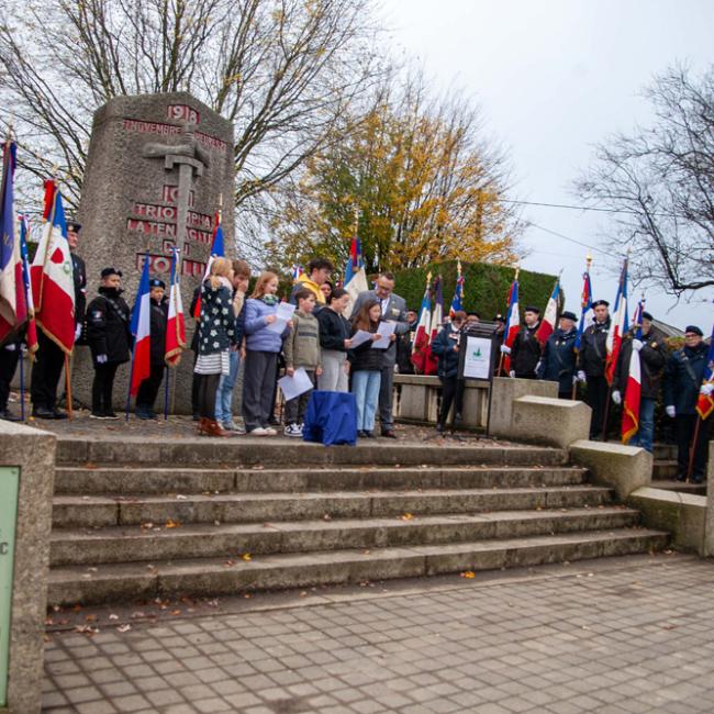 Porte-drapeaux et enfants lisant un discours devant un monument aux morts