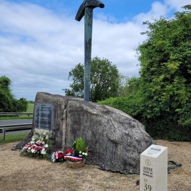 Monument en pierre surmonté d’une épée avec gerbes de fleurs et borne Aisne Terre de Mémoire au premier plan à Leuilly-sous-Coucy
